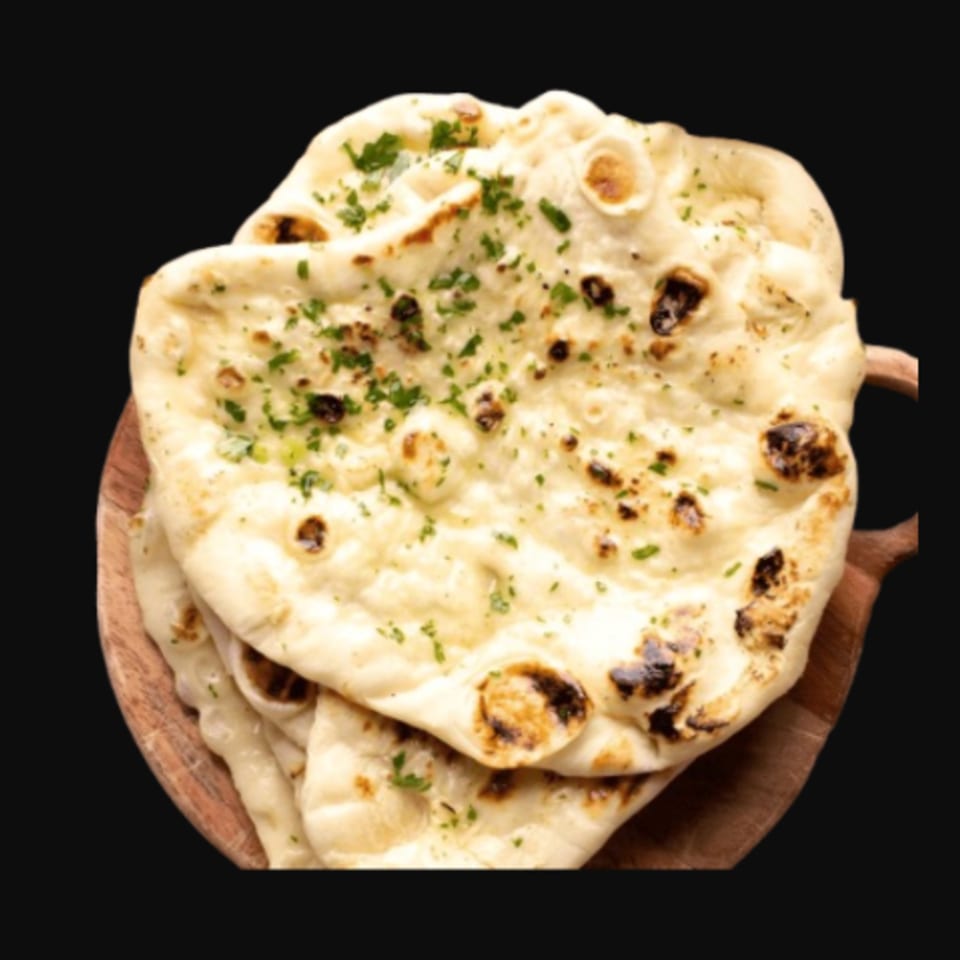 Stack of golden-brown Indian naan bread, garnished with fresh green herbs, on a wooden board.