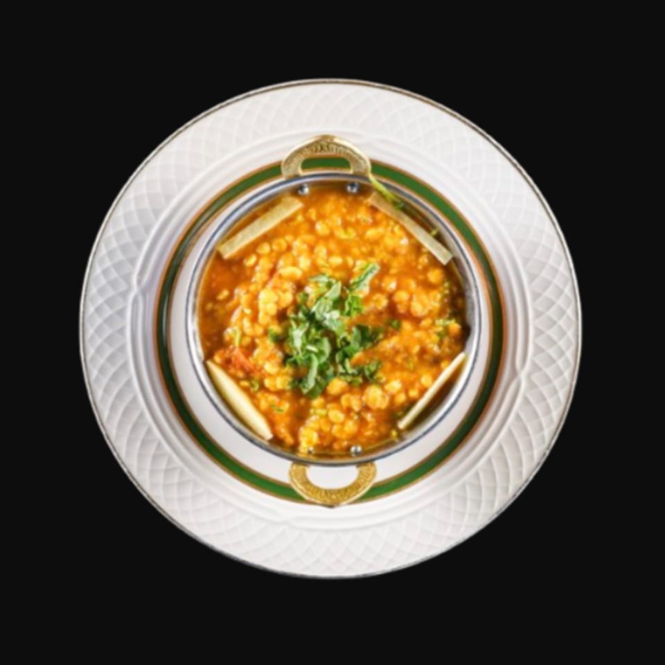 A metal bowl of Kalia Indian Cuisine's dal, garnished with cilantro, on a white and green plate.
